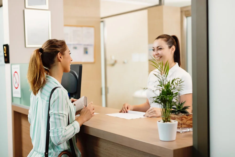 Recepcionista de una clínica atendiendo a un paciente en el mostrador